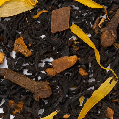 Close-up of black tea leaves with cinnamon sticks and yellow leaves on a white background